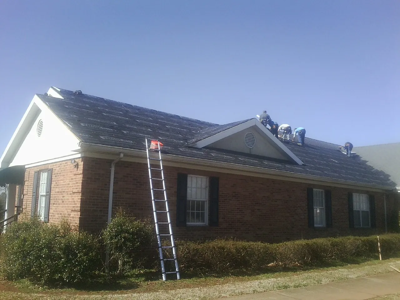 Crew tearing shingles off a brick ranch roof with a ladder set — Emergency Roof Repair work by our crew in South Plainfield