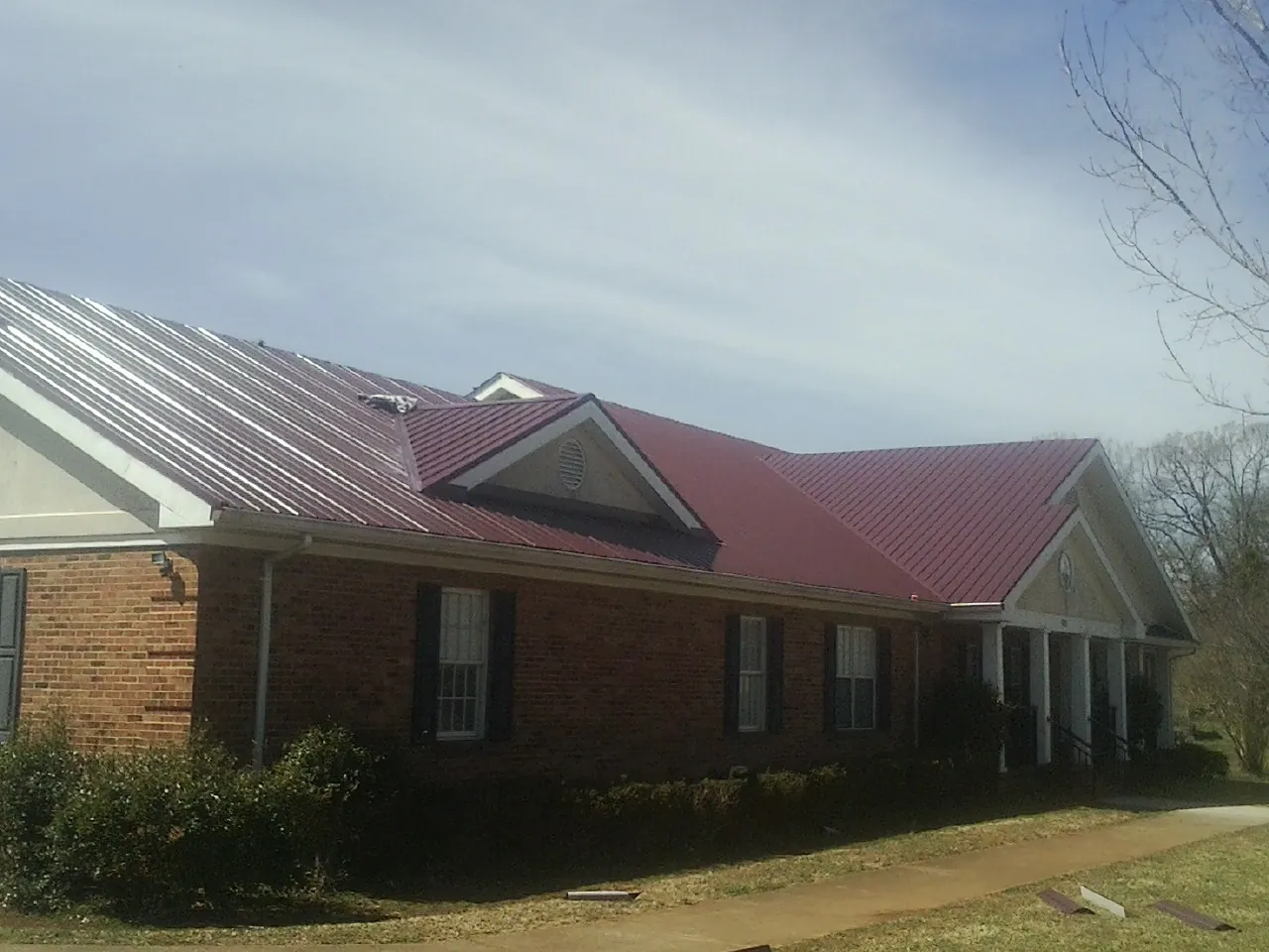 Red metal roof with gabled entries on a long brick building, from a Hail Damage Roof Repair job in South Plainfield