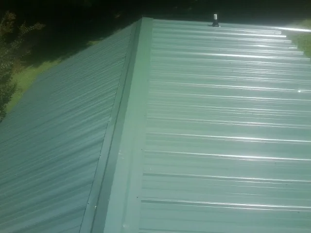 New green metal panels meeting at the ridge of a roof — Flat Roof Repair work by our crew in South Plainfield