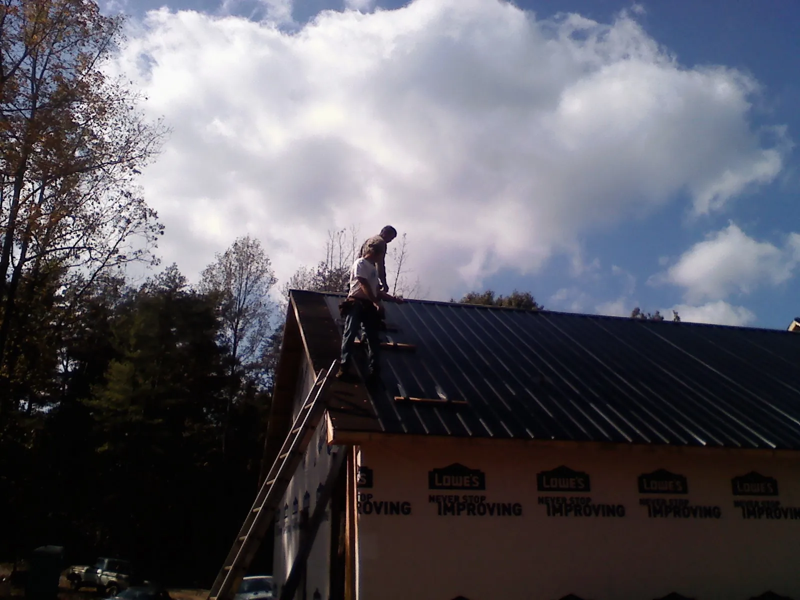 Roofer fastening dark metal panels high against a cloudy sky, from a Roof Inspection job in South Plainfield