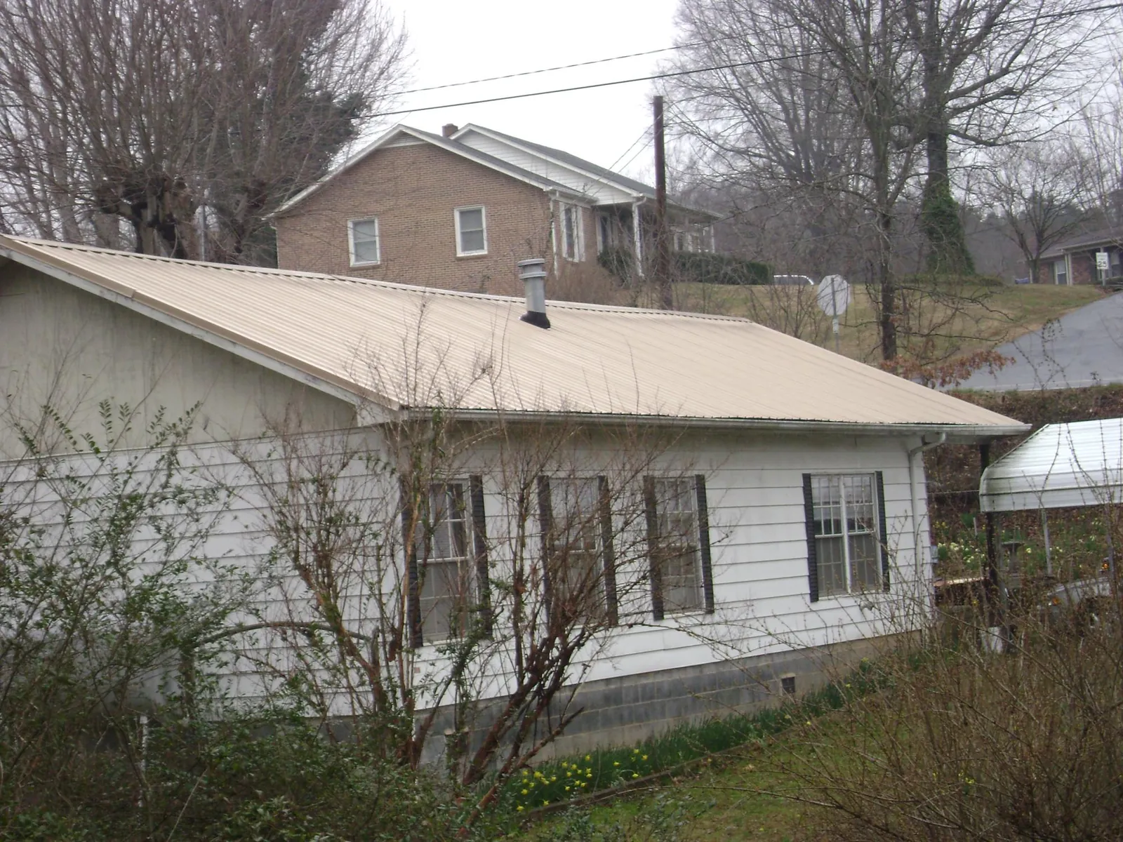 Tan metal roof on a white sided house set into a hillside — Commercial Roofing by Roofing Brothers in South Plainfield